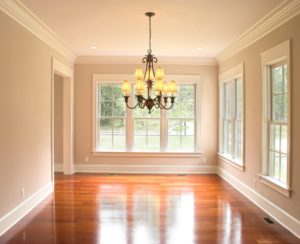 View of empty room in a home with wood flooring, an elaborate chandelier, and three white-frame windows. 