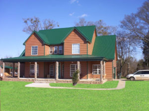 Exterior view of home with large front lawn, elaborate porch pillars, and green metal roofing.