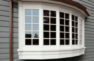 Close-up view of home with gray house siding and white bay window.